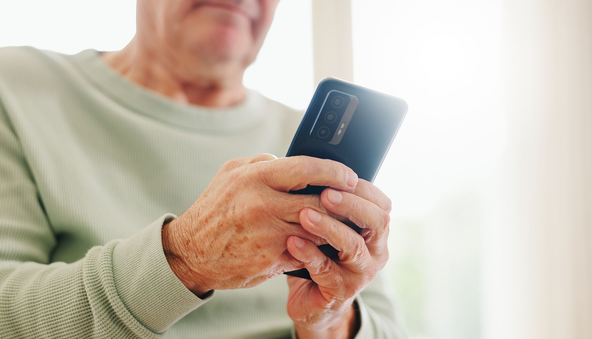 An elderly man is holding a cell phone in his hands.