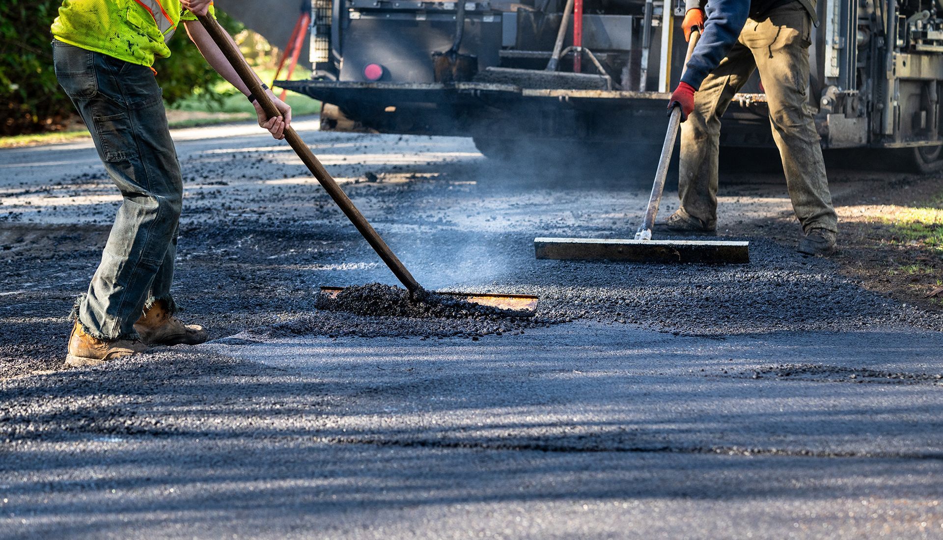 Two men are sweeping the asphalt on a road.