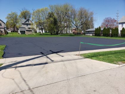 A black asphalt driveway is being installed in a residential neighborhood.
