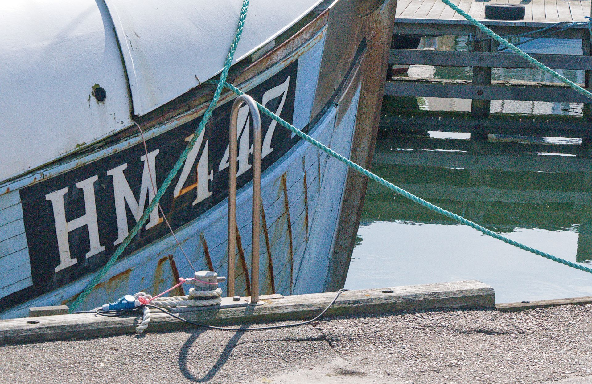 Boot aangemeerd in een jachthaven, met groene touwen aan de boeg en water ernaast.