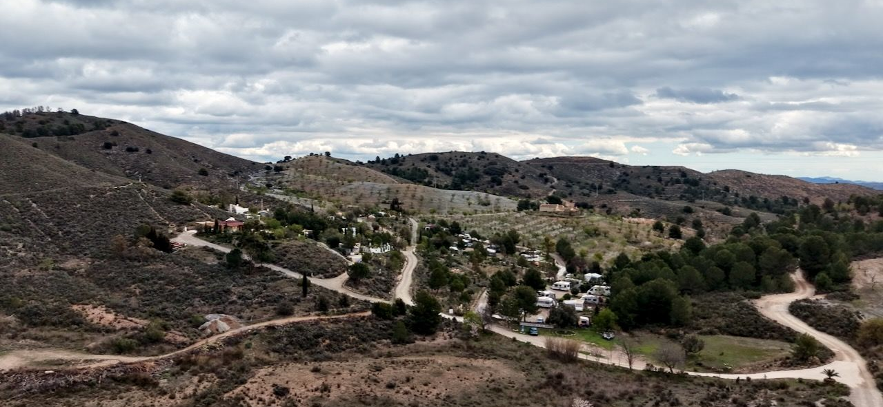Kronkelende zandwegen door een droog, heuvelachtig landschap onder een bewolkte hemel.