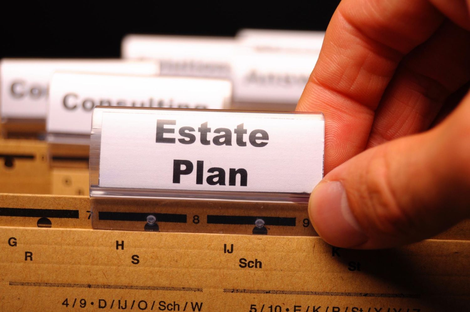 Hand placing an “Estate Plan” tab in a file organizer with labeled folders.