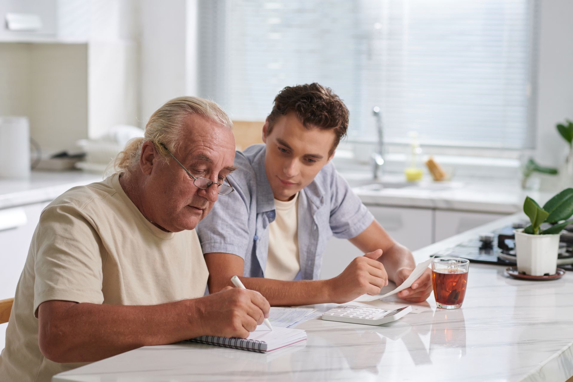 Two people reviewing paperwork at a kitchen table with a notebook and glass of iced tea