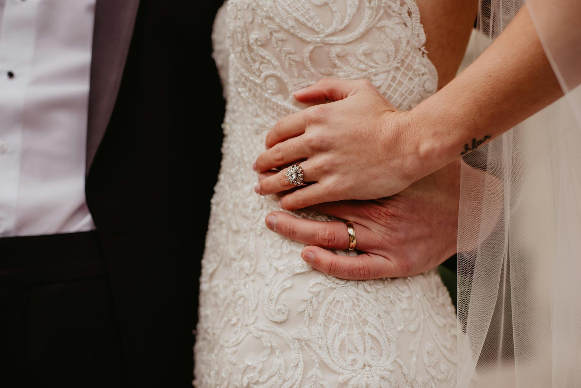 Bride and partner holding hands at waist, showing wedding rings and lace gown detail