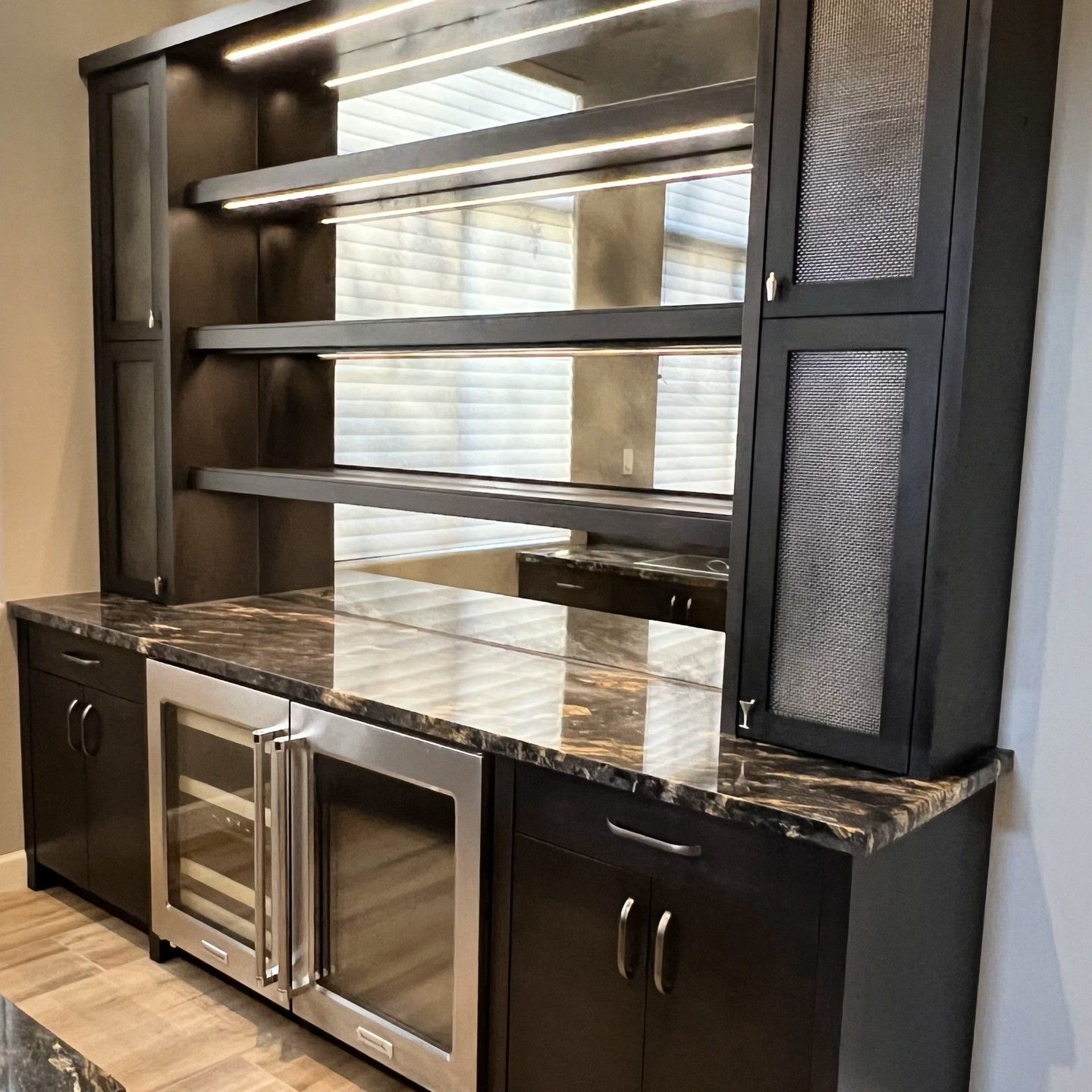 A dark wood home bar with a marble countertop, mirrored backsplash, lighted shelves, and dual glass-door beverage coolers.
