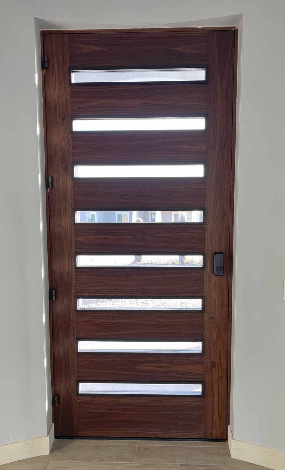 A dark wood front door with eight horizontal frosted glass panels, set in a light-colored wall.