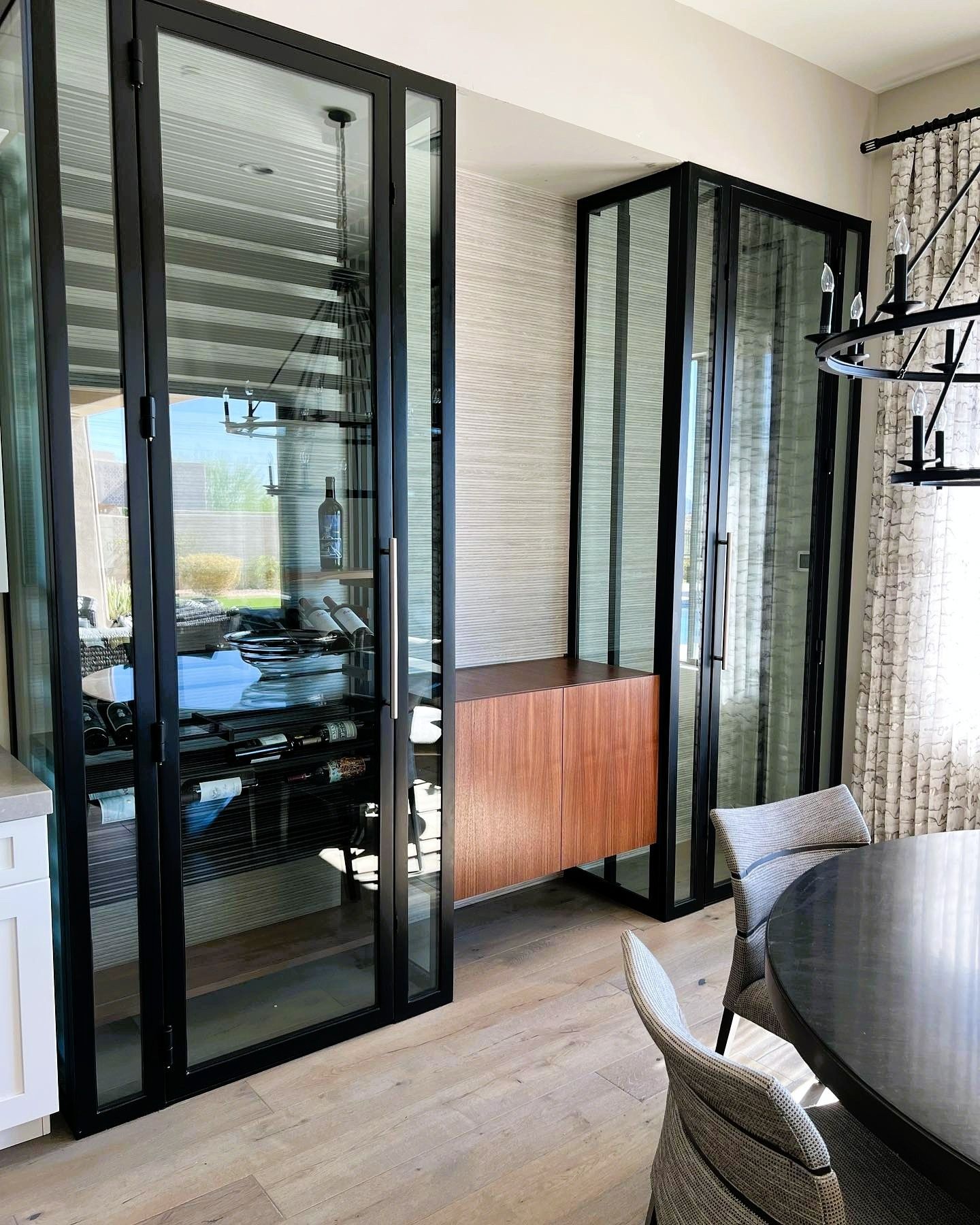 Tall black-framed glass wine cabinets with a wood sideboard between them in a contemporary dining room.