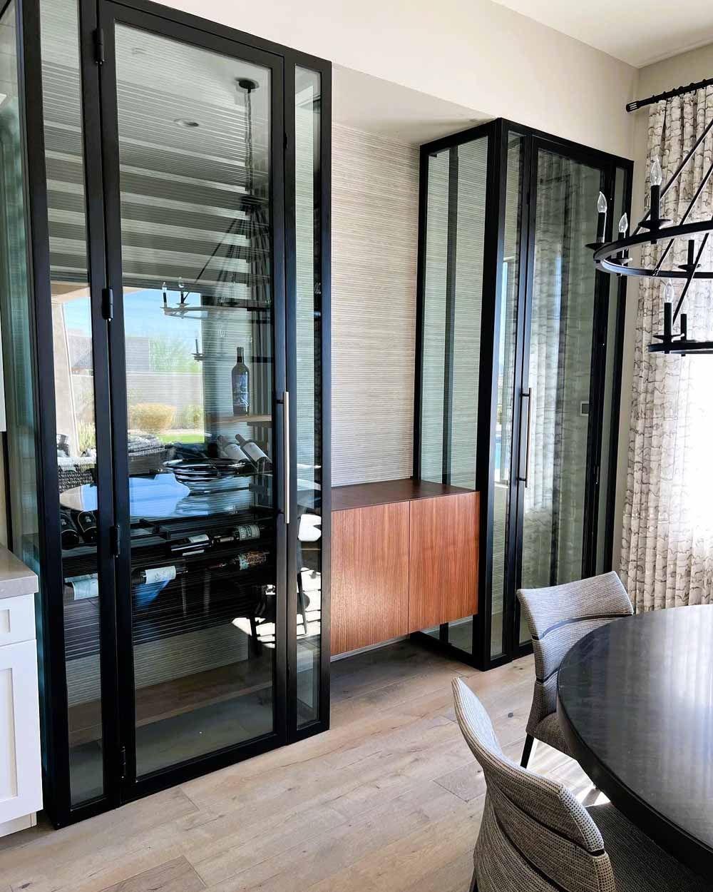 Two tall, black-framed glass cabinets flank a central wooden sideboard against a textured wall in a modern dining room.