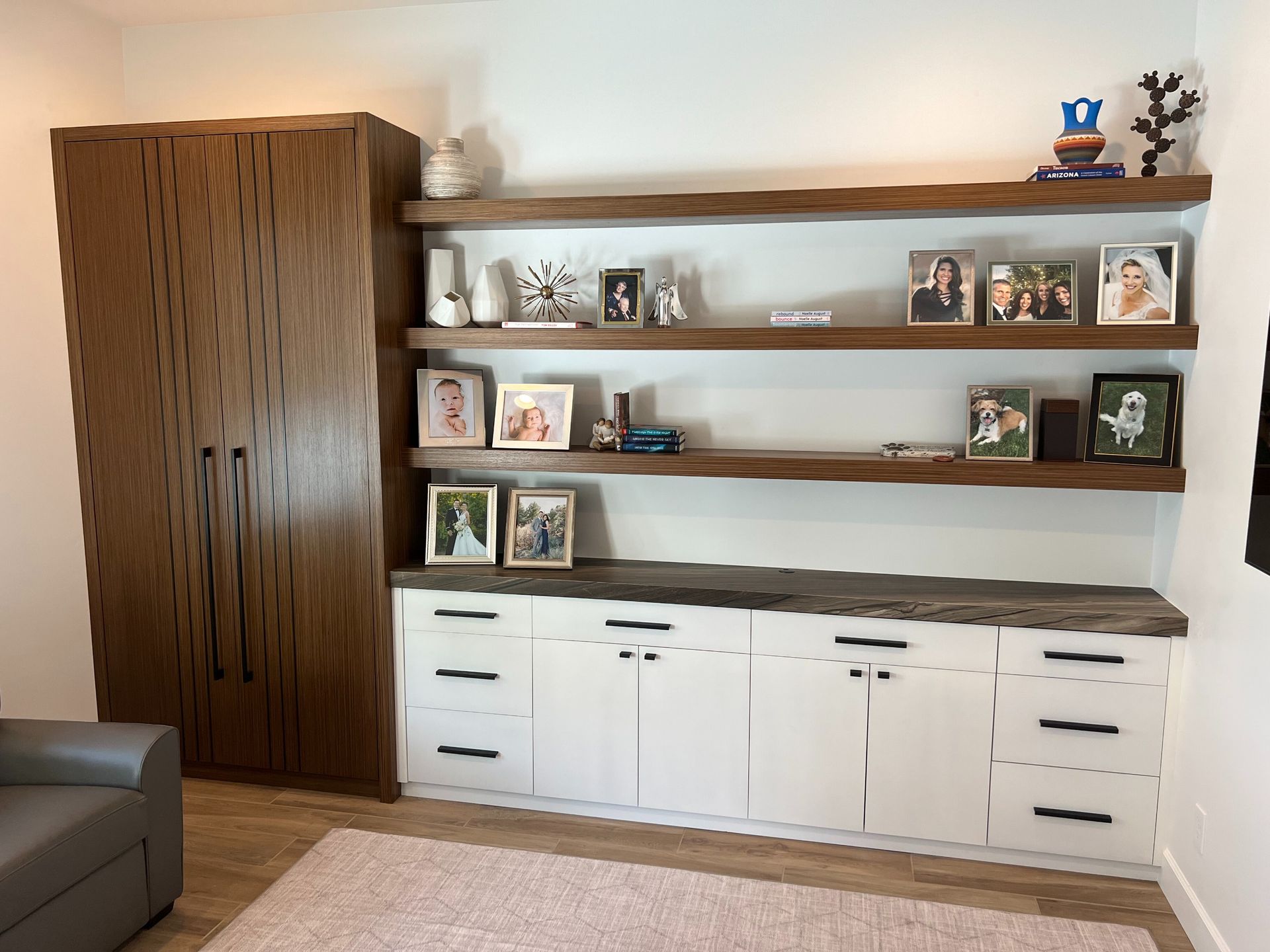 A wood-grain cabinet stands next to white lower cabinets and three open shelves holding framed photos and decor.