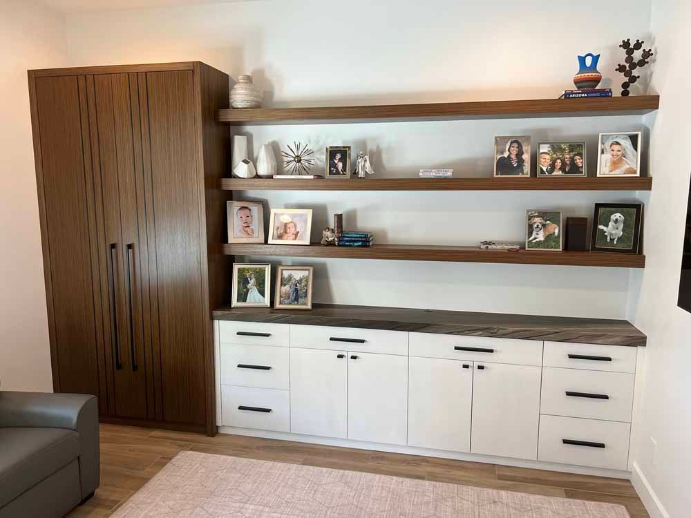 A tall wooden cabinet next to a white storage unit with three floating shelves displaying photos and decor items.