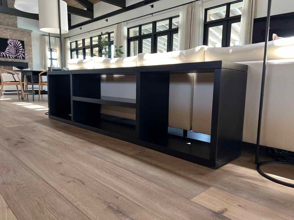 A long, black open-shelving console table sits on light wood flooring behind a white sofa in a bright, modern living room.