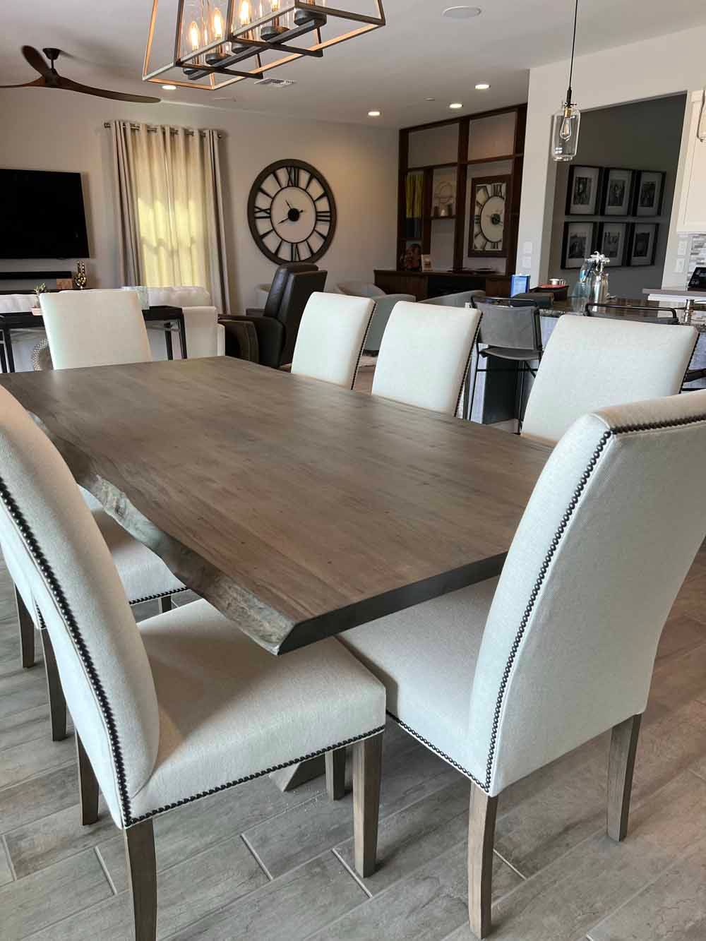 A dining area with a rustic wooden table surrounded by six off-white upholstered chairs, under a modern farmhouse lamp.