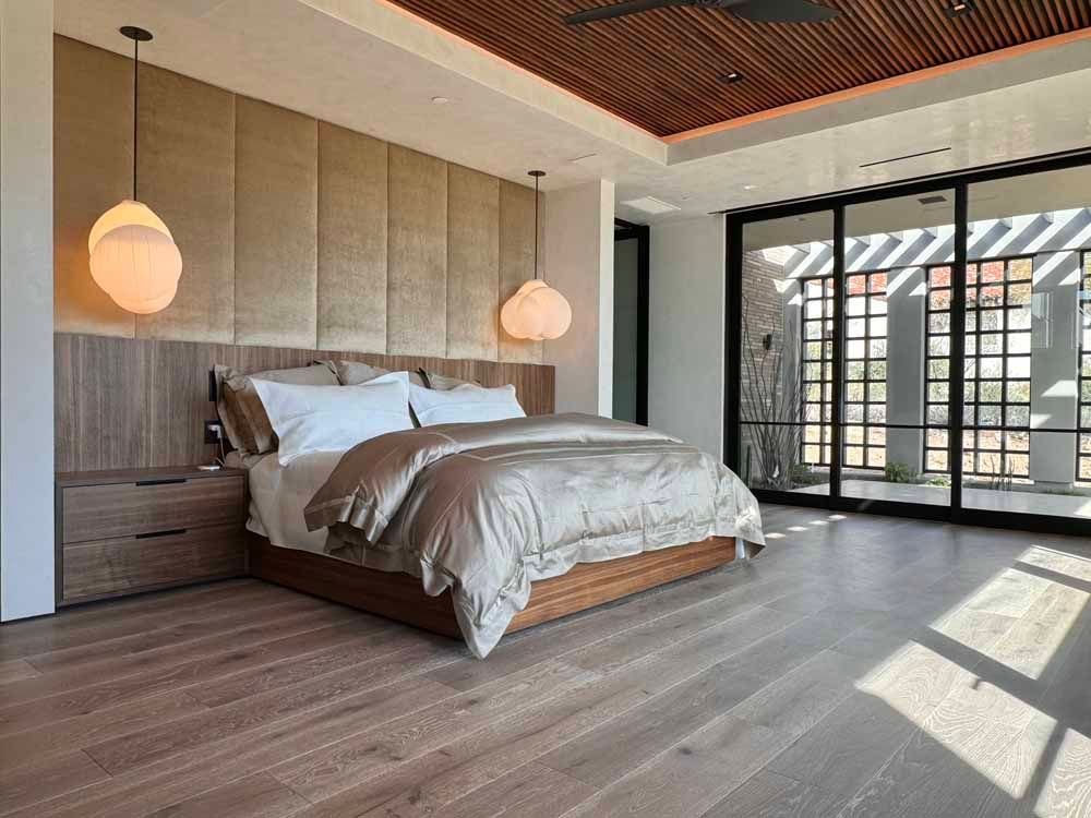 A modern bedroom with a tufted headboard, low wooden bed, globe pendant lights, and large glass doors to a patio.