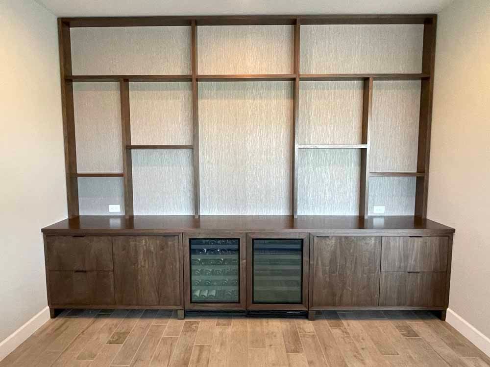 Built-in dark wood shelving and cabinetry with two glass-front wine coolers, set against a textured light gray wall.