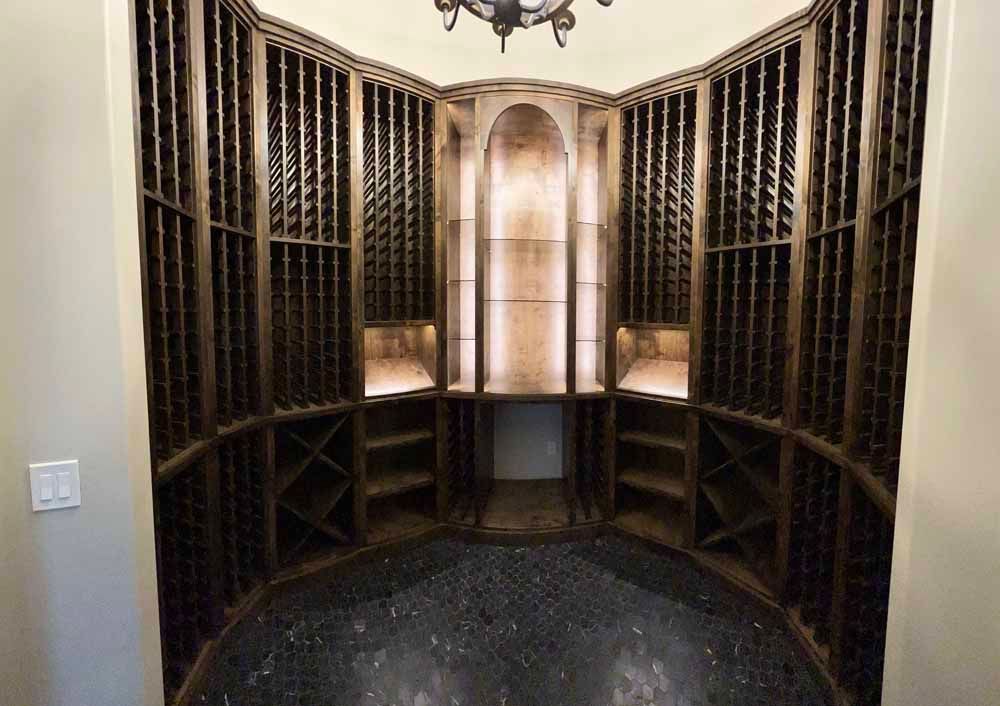 A custom, dark wood wine cellar featuring floor-to-ceiling bottle storage, a central display alcove, and dark tile flooring.