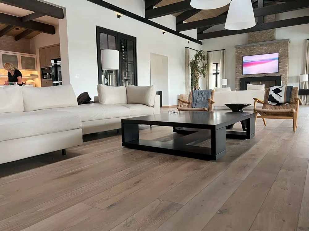 Spacious living room with a white sectional sofa, black coffee table, wood floors, and exposed ceiling beams.