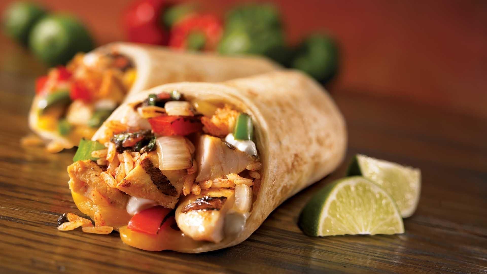 Burrito filled with chicken, rice, and vegetables, with lime wedges on a wooden table.