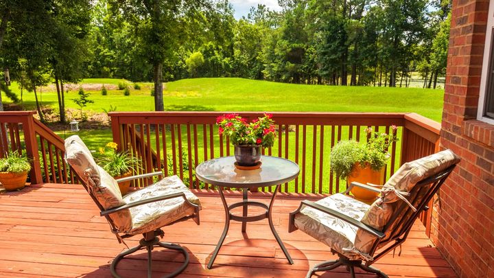 New deck on the back of a house.  The deck is overlooking a large backyard.  There is a small patio furniture set on the deck.