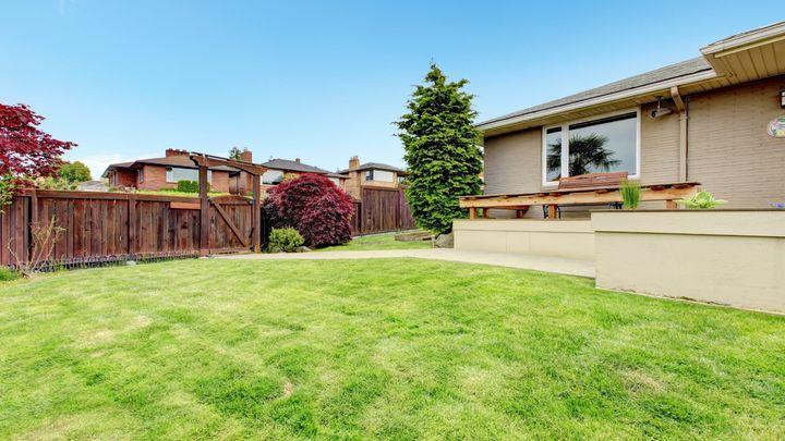Backyard of a residential property.  The backyard has a patio and is enclosed by a wooden fence.