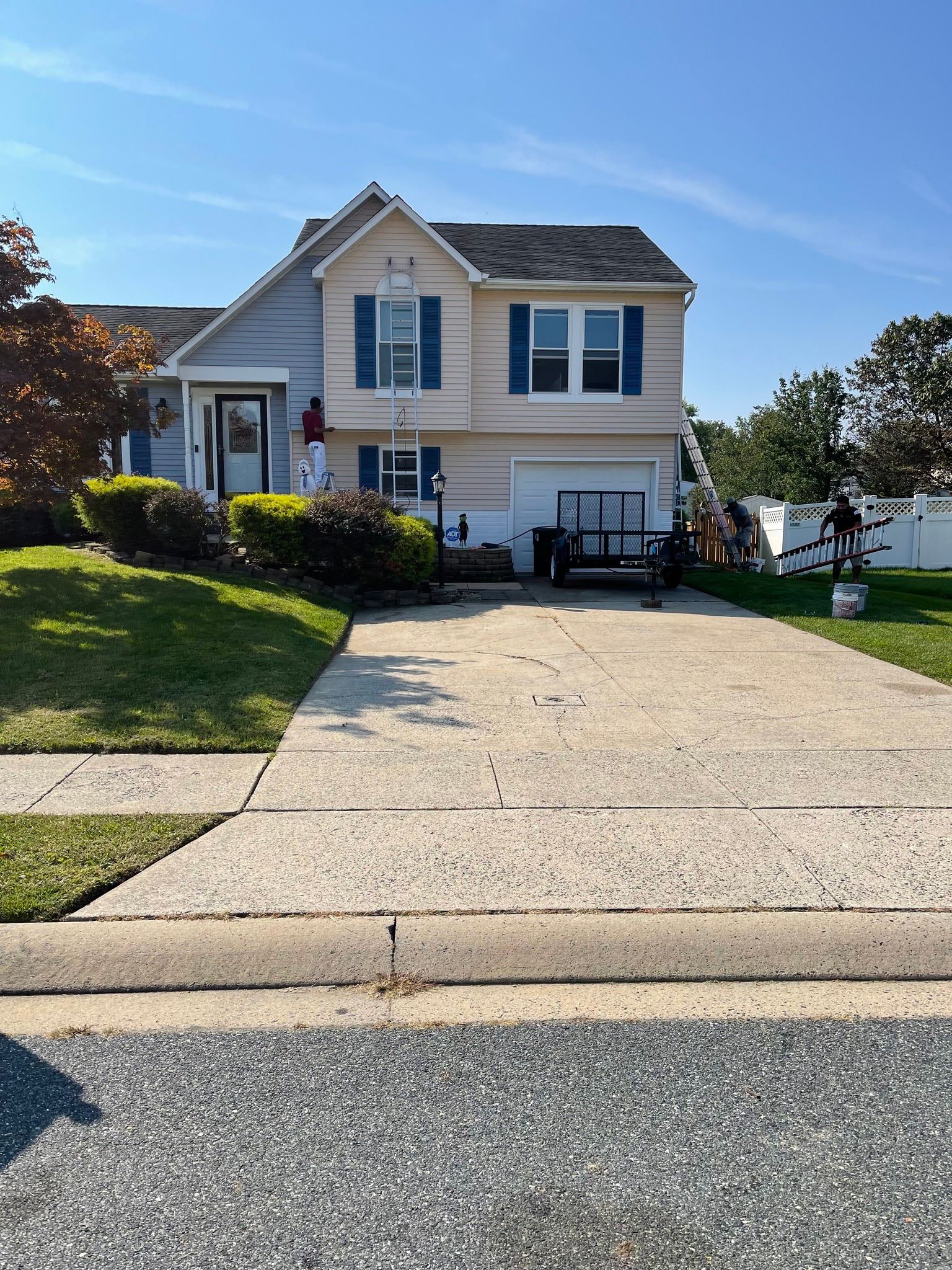 Suburban house with blue shutters, front lawn, and wide concrete driveway under a clear sky