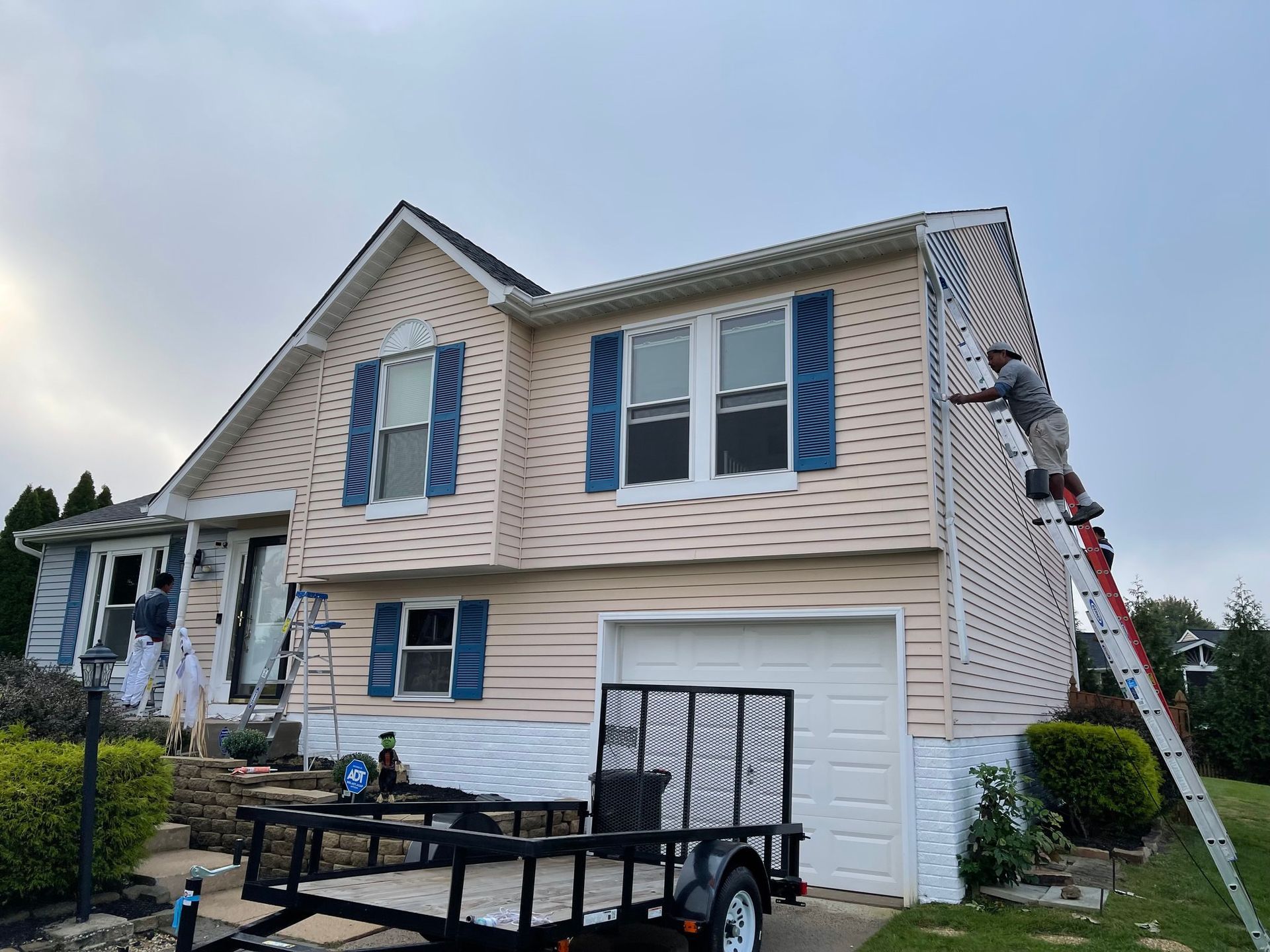 Suburban house with beige siding and a person on a ladder cleaning the upper wall