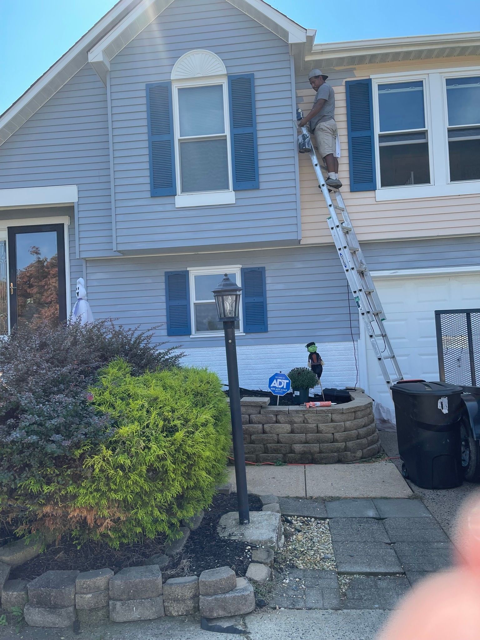 Exterior of a blue house with a ladder leaning against the second floor and a person near the front steps