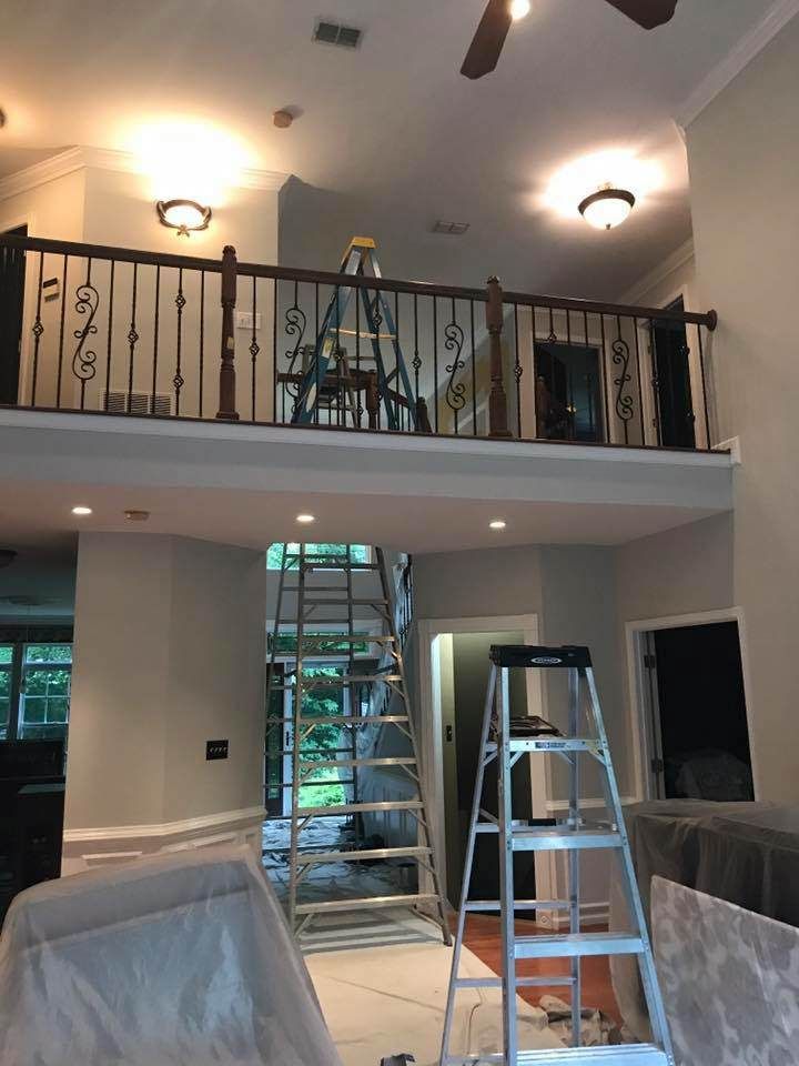 Two-story room under renovation with ladders, scaffolding, and covered furniture on the floor