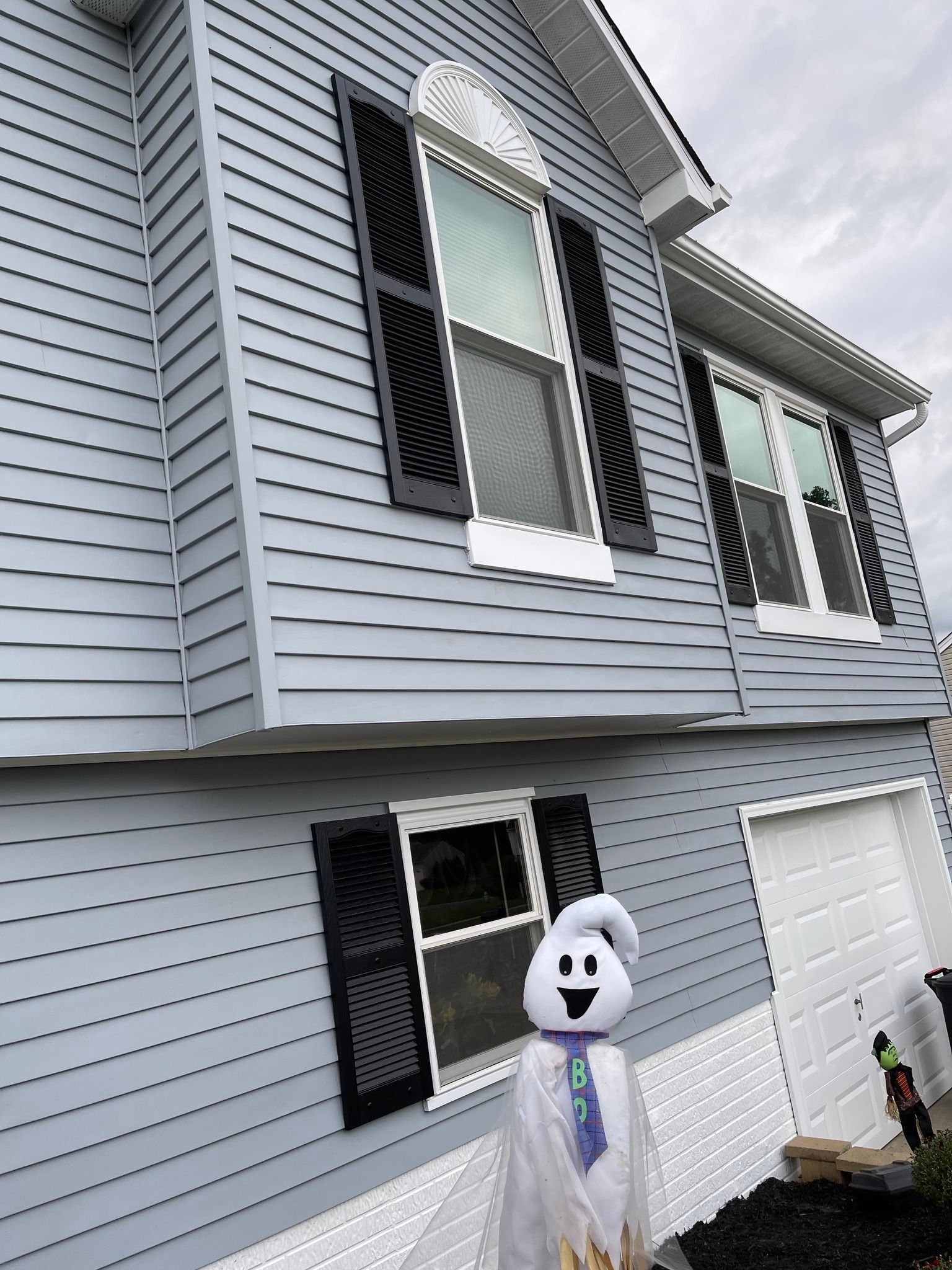 House exterior with gray siding and black shutters; a ghost decoration hangs near the front window.