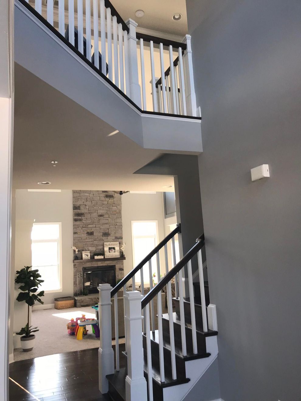 Modern home interior with gray walls, white railings, staircase, and a living room in the background