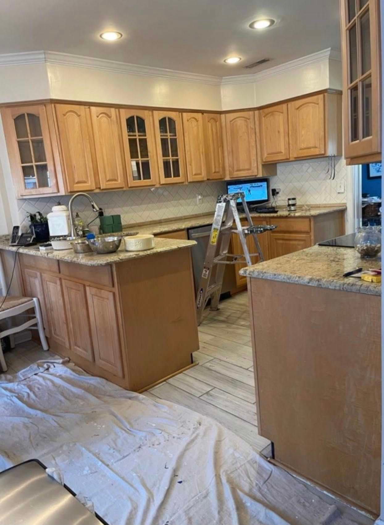 Kitchen under renovation with wooden cabinets, granite counters, a ladder, and a covered floor area