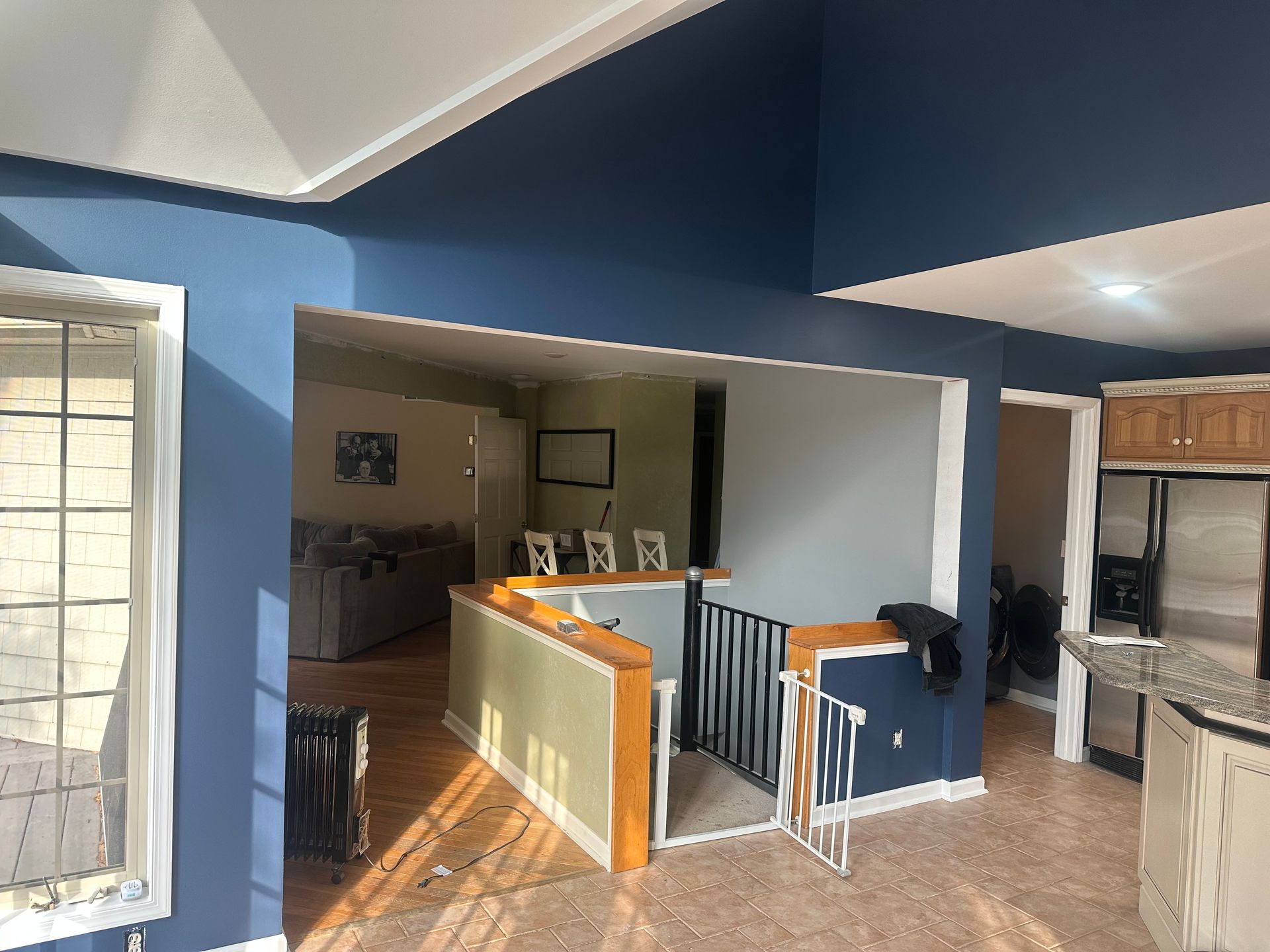 Open-plan kitchen and living area with blue walls, white trim, and a breakfast bar beside a staircase.