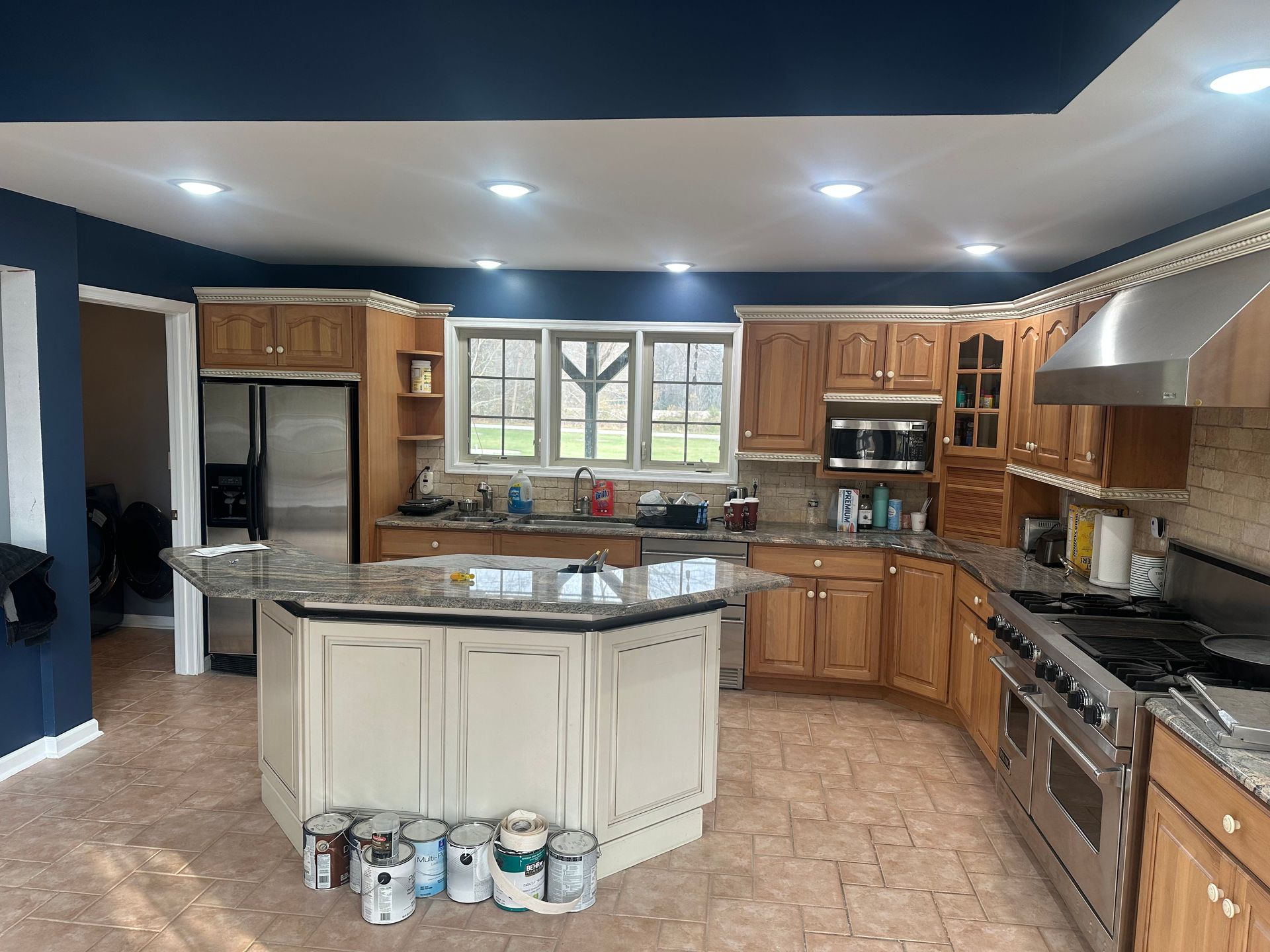 Spacious kitchen with wooden cabinets, central island, stainless appliances, and blue walls.
