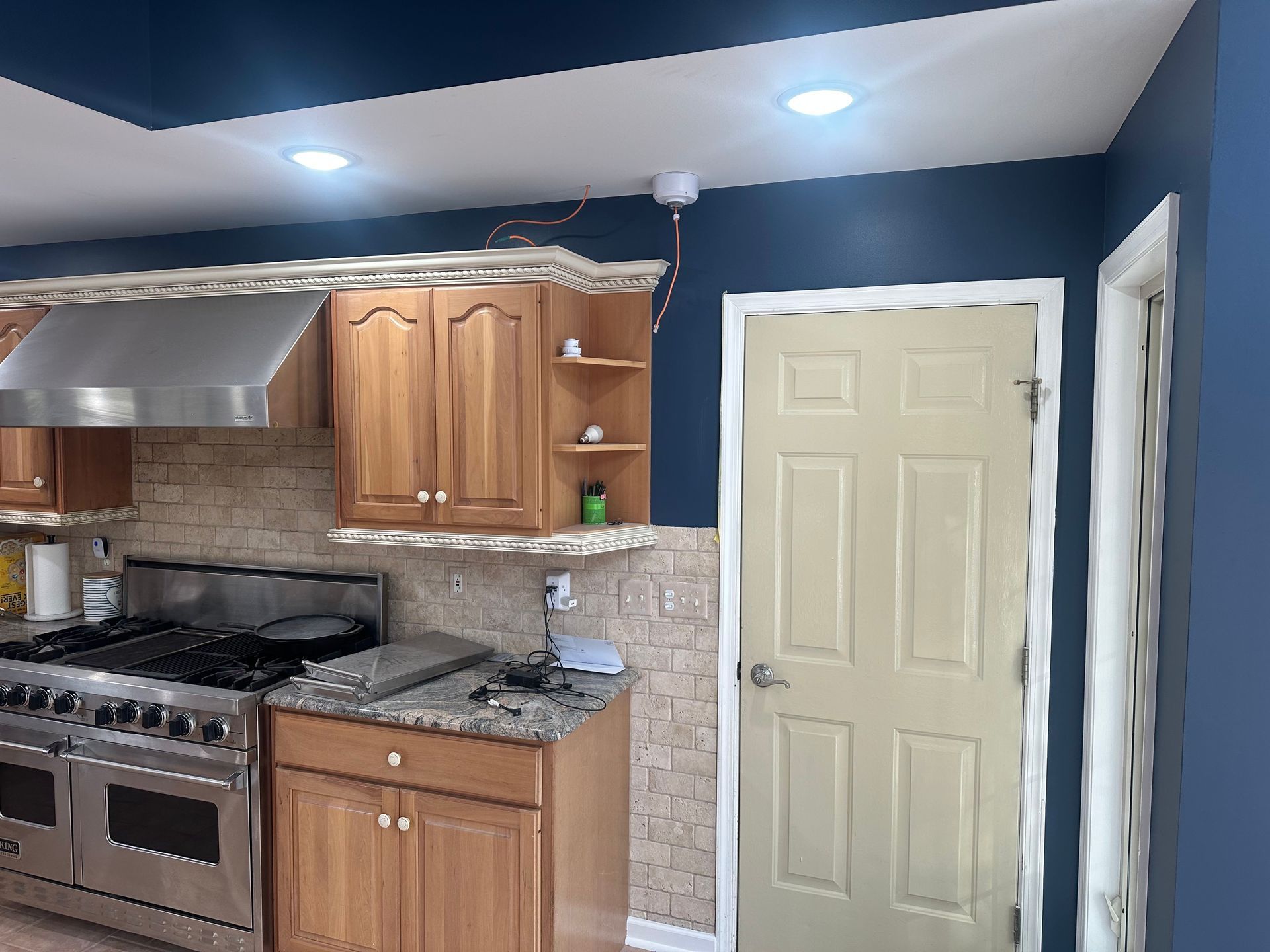 Modern kitchen with beige cabinets, stainless stove, granite counters, and a cream door against dark blue walls