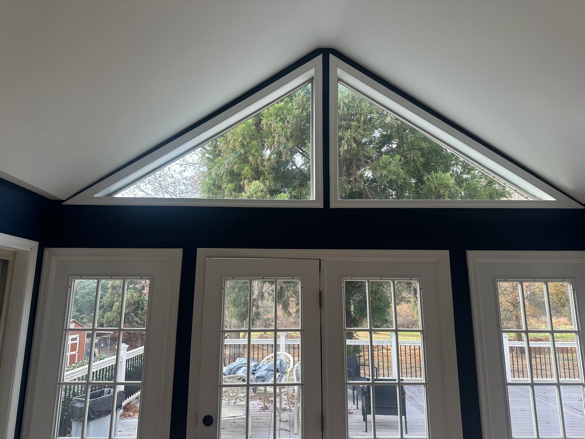 Interior with blue walls, white French doors, and a triangular window above showing trees outside