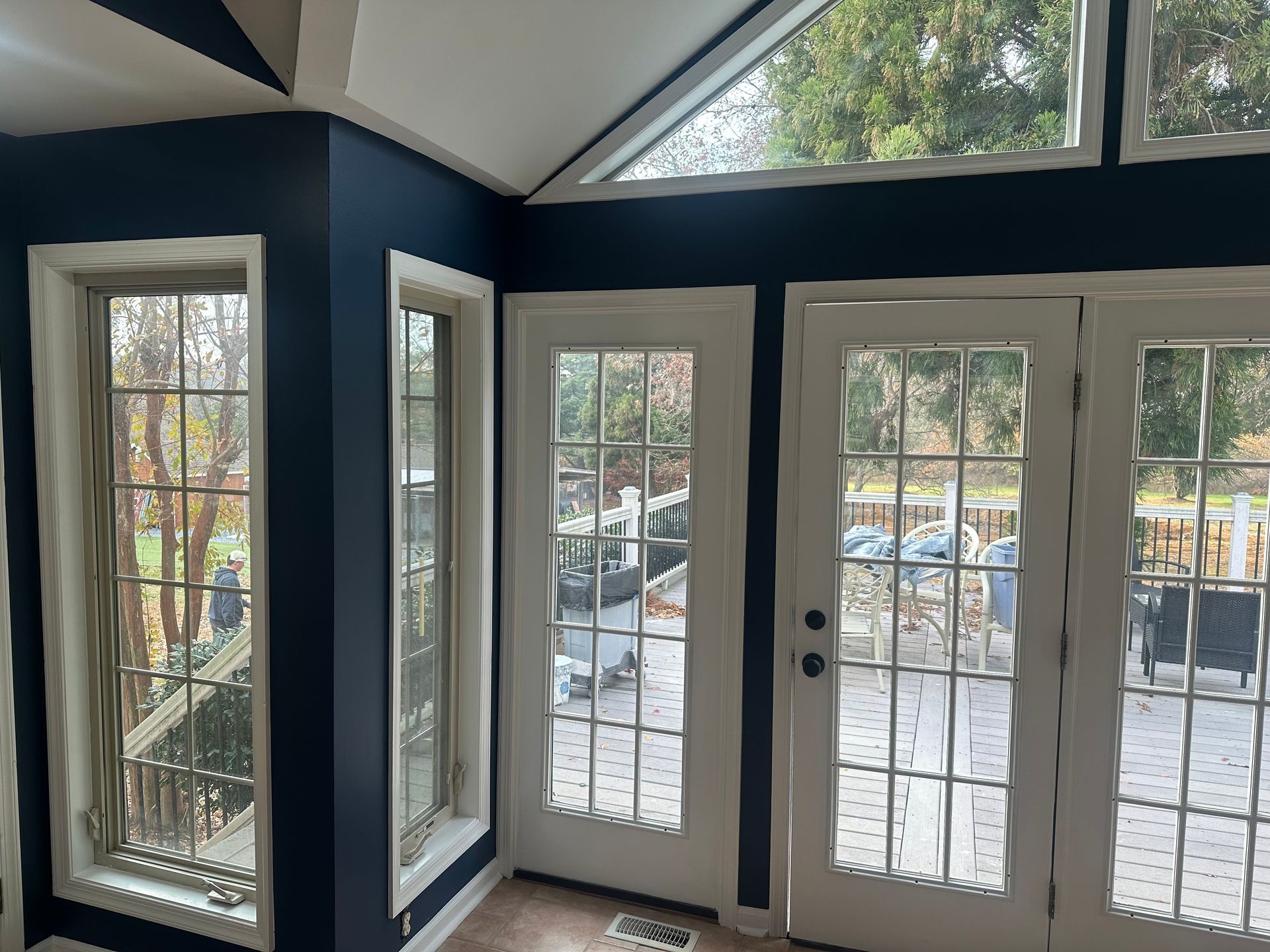Bright sunroom with navy walls, tall windows, and French doors overlooking a patio and parked cars