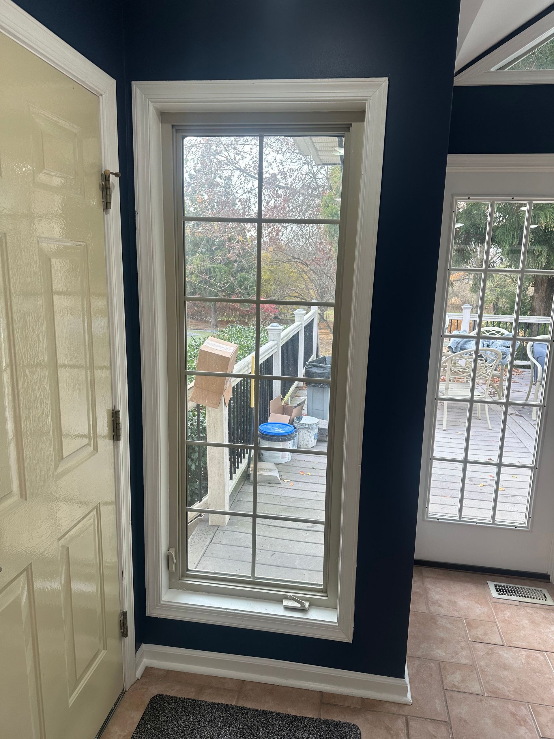 Foyer with navy walls, white door and trim, and two tall windows overlooking a porch and yard.