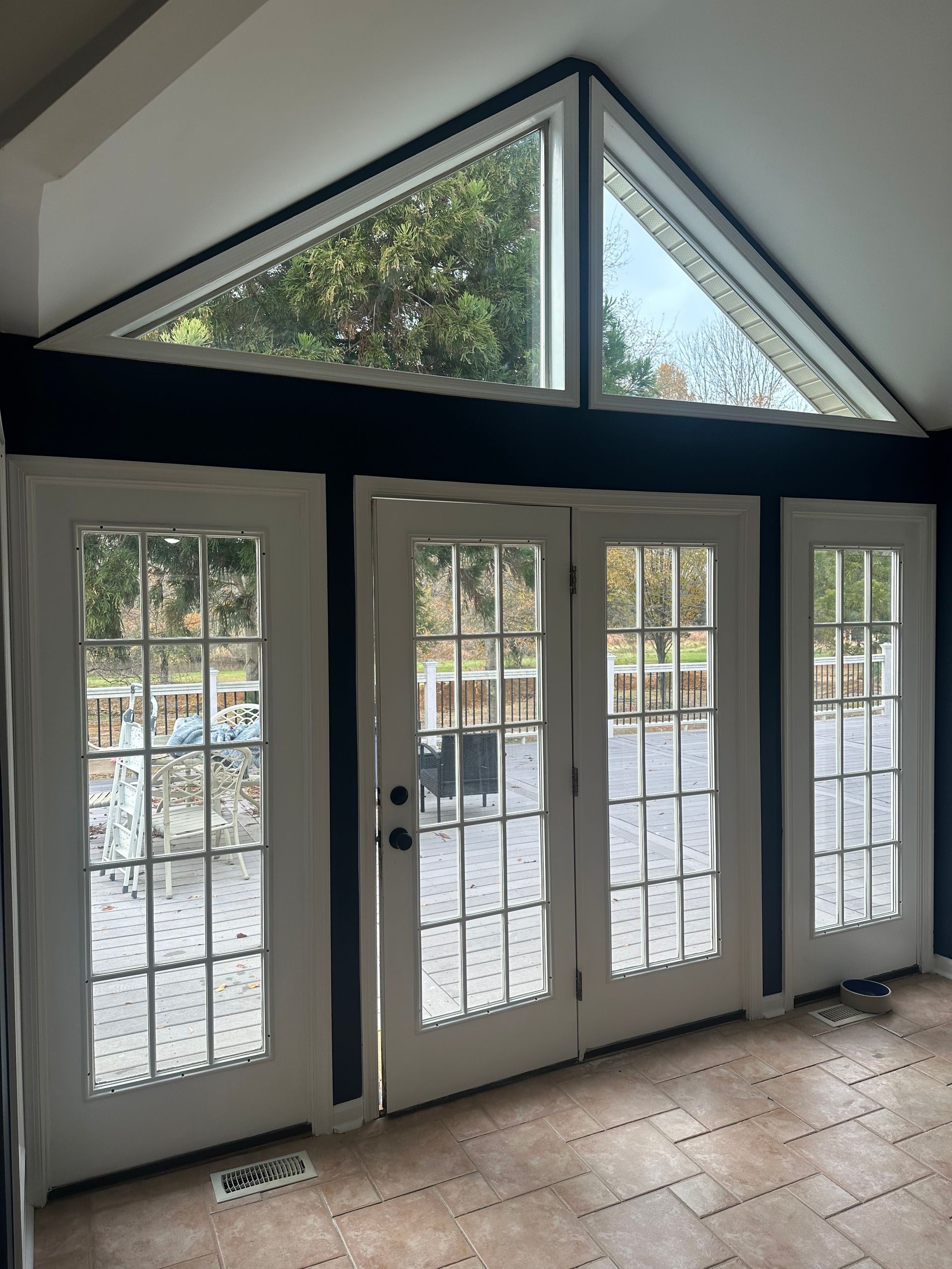 Tall front entry with white French doors, sidelights, and triangular windows above, showing a snowy outdoor view.