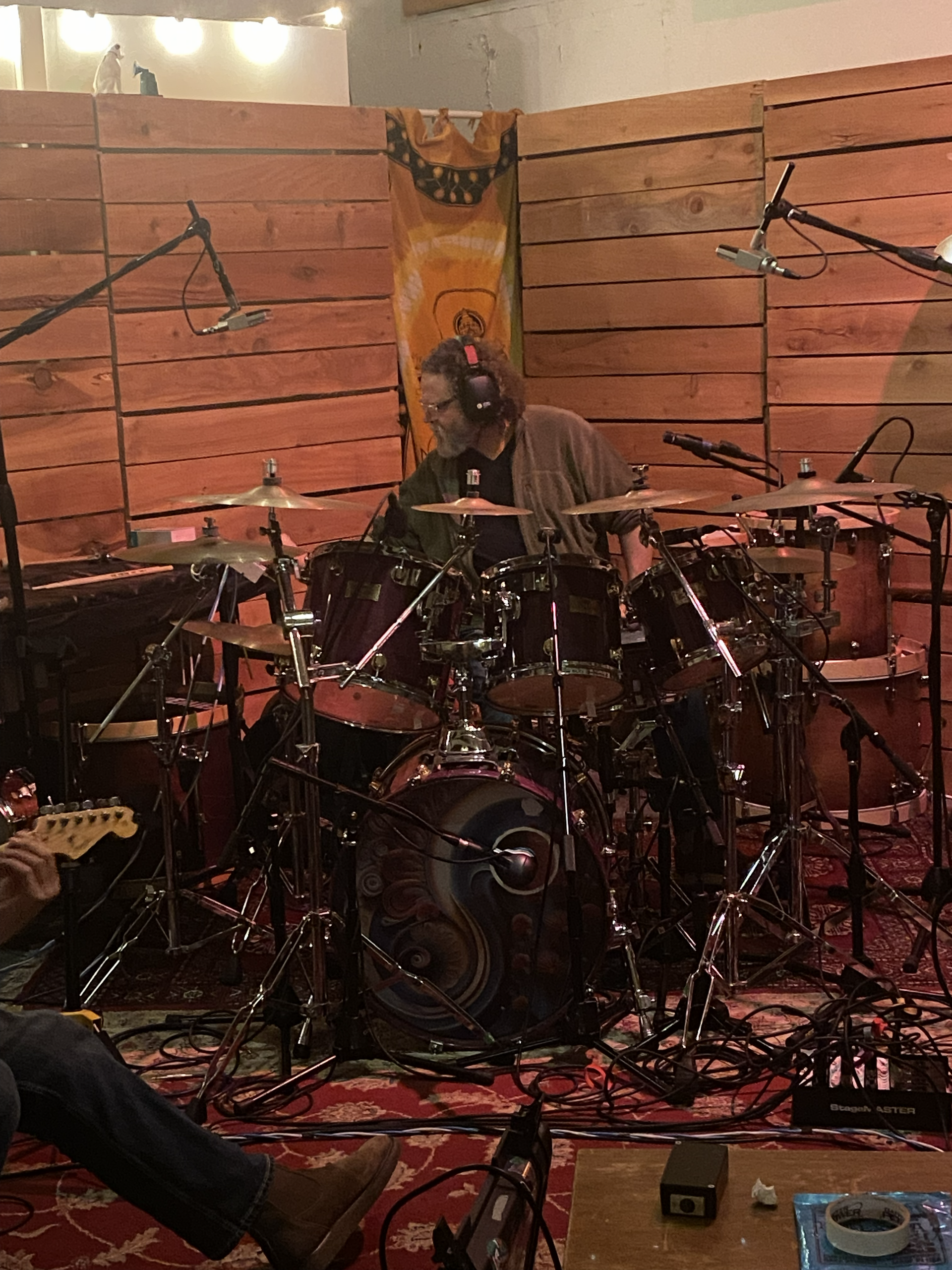 Drummer performing in a recording studio, surrounded by microphones and a drum kit under warm wood-paneled lighting