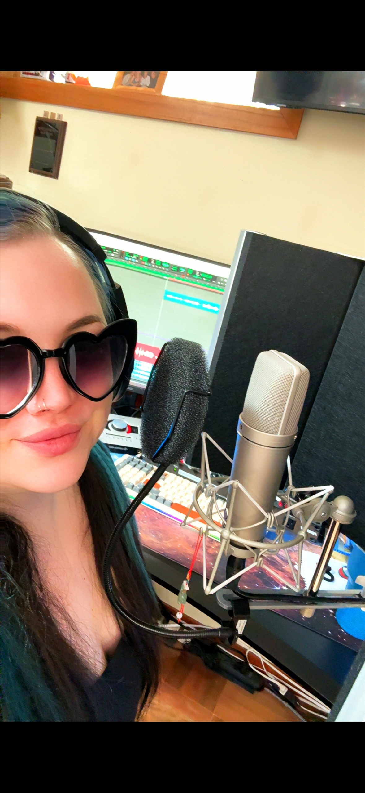 Woman wearing sunglasses beside studio microphones and a computer screen in a recording setup