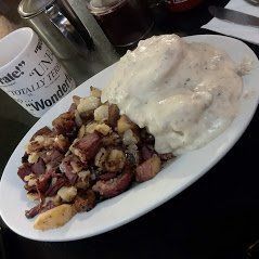 Plate of biscuits and gravy beside crispy breakfast potatoes on a diner table