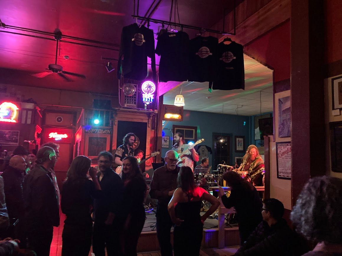 People mingling in a dimly lit bar with pink and purple lighting and hanging decorations.