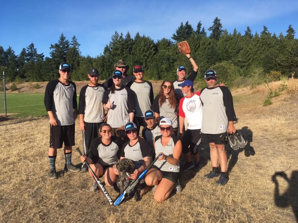 Group of people posing outdoors on a dirt field with sticks, trees and blue sky in the background.