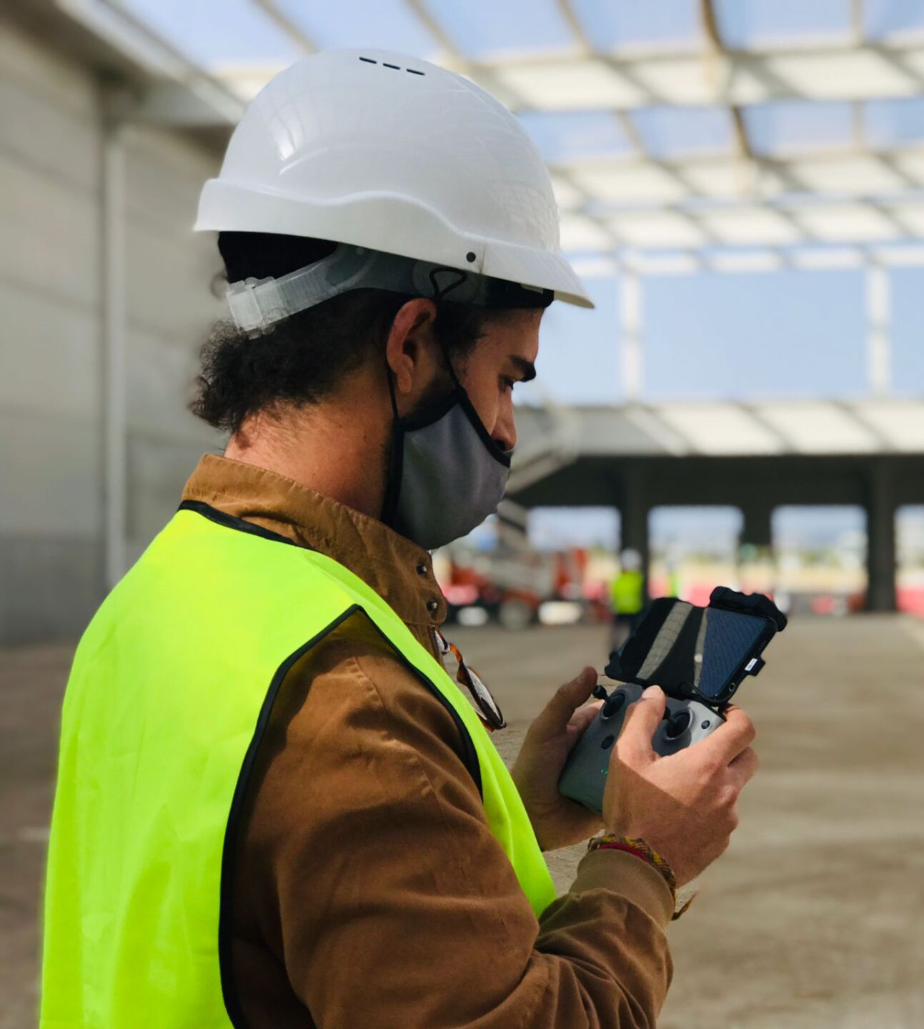 Trabajador con casco y chaleco de seguridad usando una tableta en una obra de construcción.