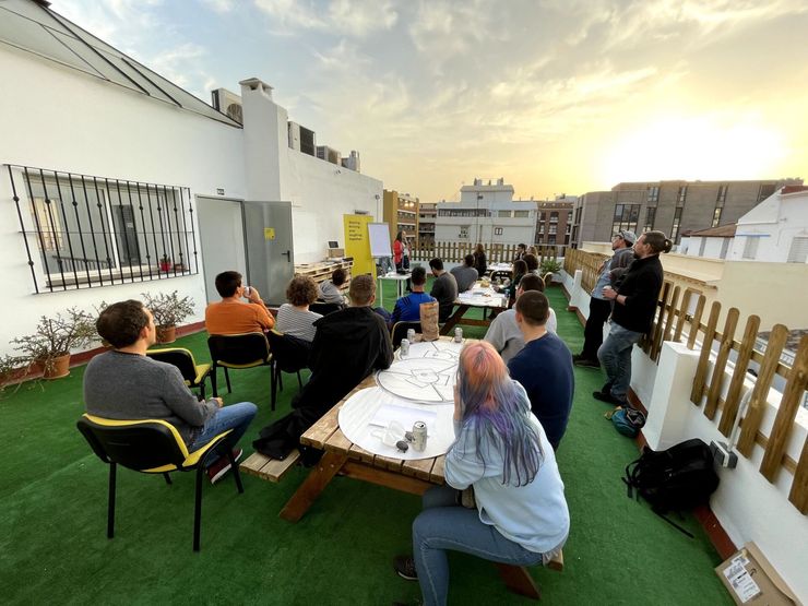 Gente sentada al aire libre en mesas en una terraza en la azotea al atardecer, con vistas a la ciudad.
