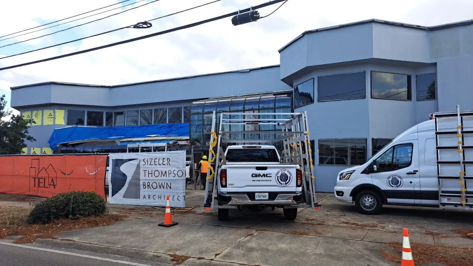 Building under construction. White truck with glass rack in front. People and a van are present.