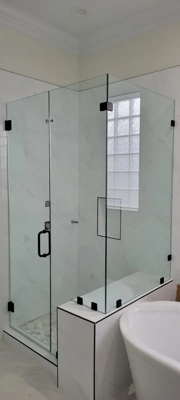 Glass shower enclosure in a bathroom with a white tub.