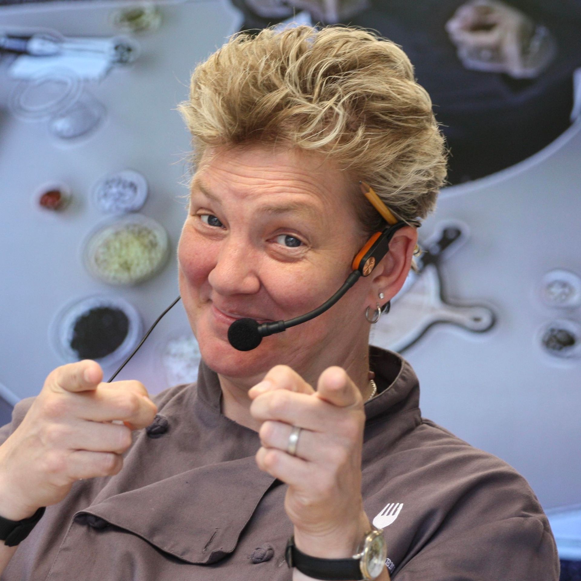 Headset-wearing presenter pointing at the camera with a playful smile, in a studio setting