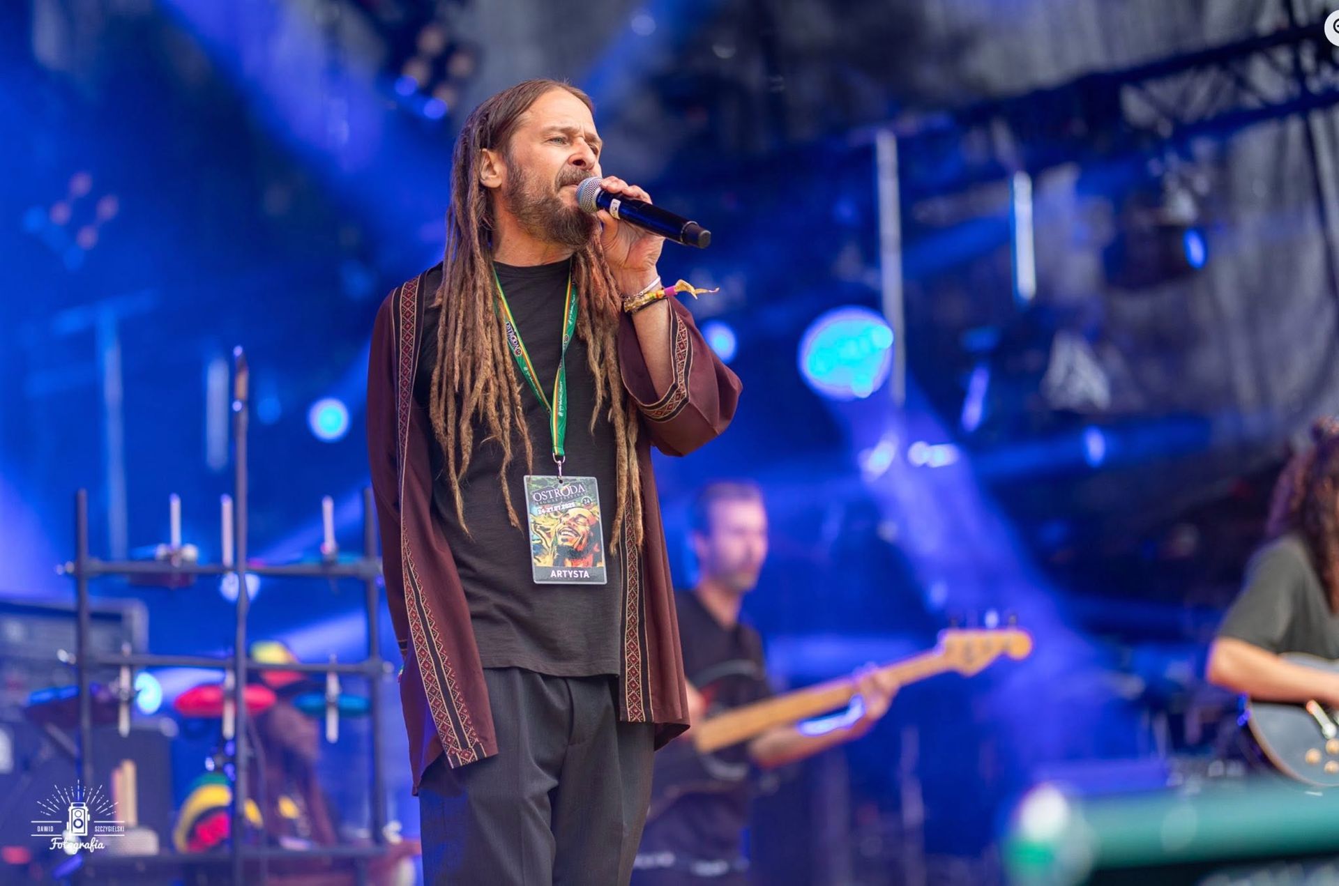 Singer performing onstage with microphone, band and blue stage lights in the background