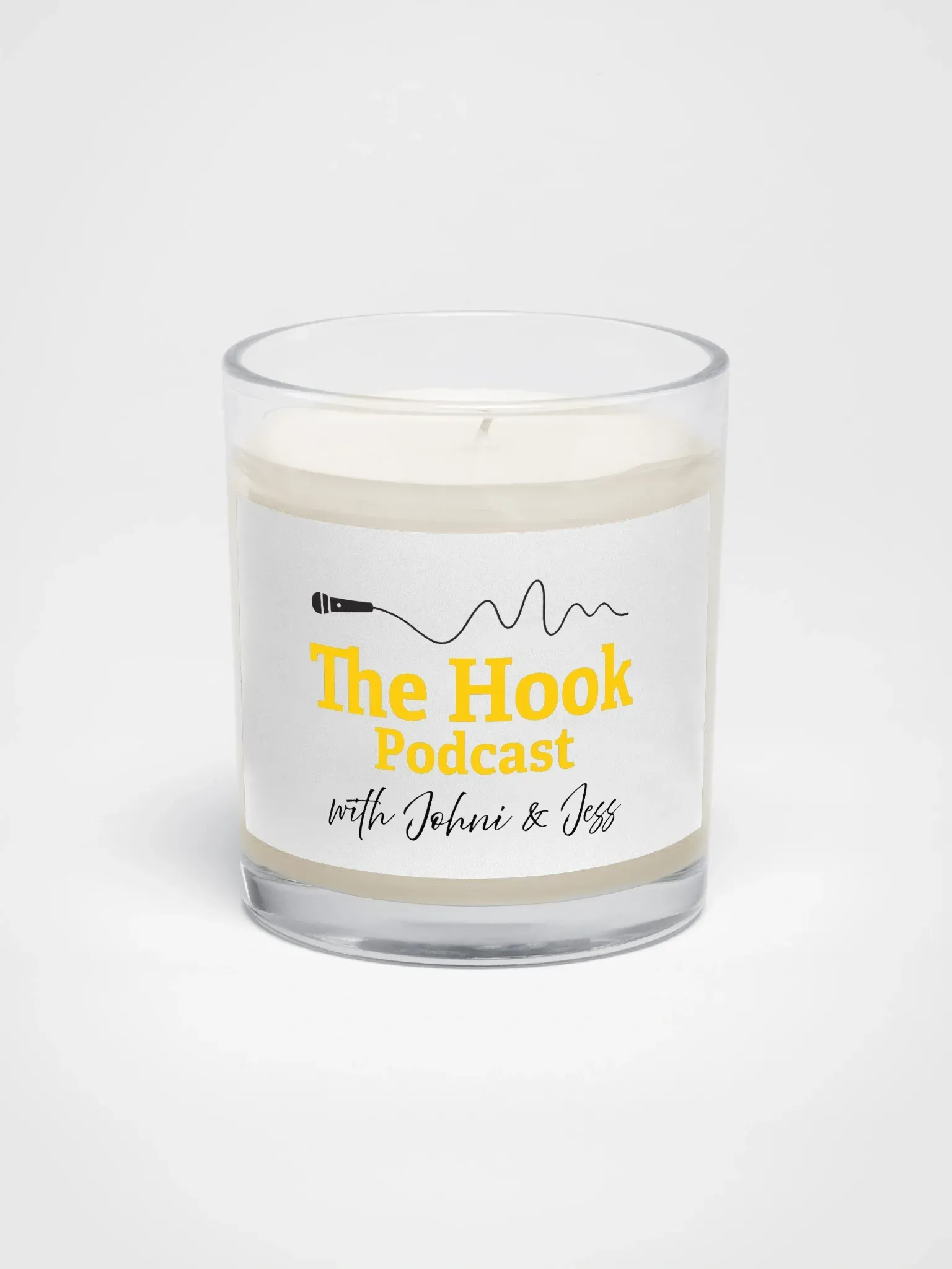 White candle in a clear glass jar labeled “The Hook Podcast” on a light background