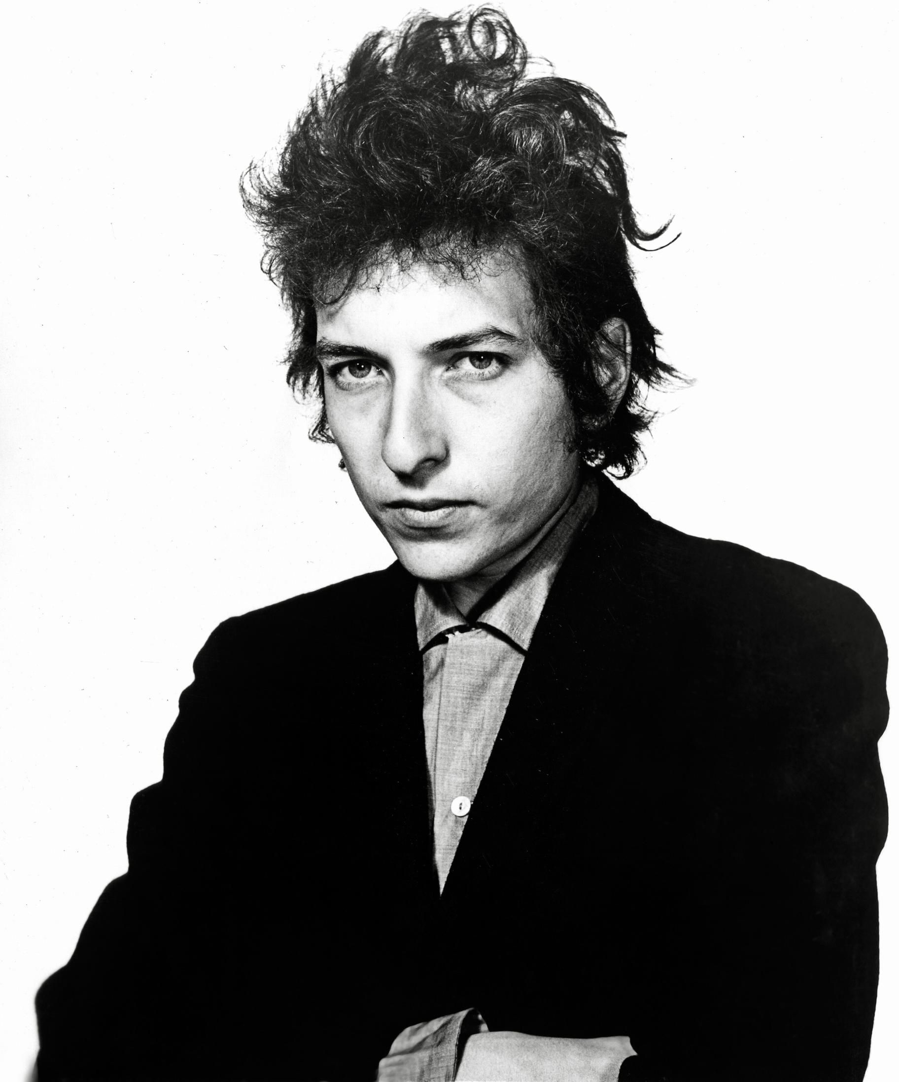Bob Dylan in a black suit, staring intently.  He has curly, messy hair.